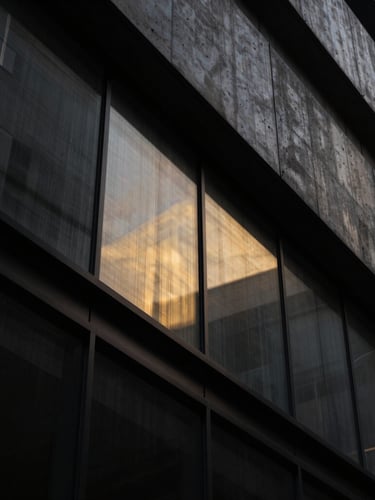 Dramatic low-key architectural crop of a modern concrete and glass facade, sharp diagonal lines, metallic gold light leaks reflecting on dark steel, 35mm lens
