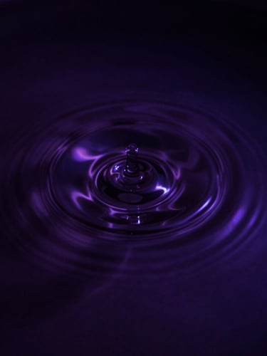 Moody dark-mode photography of a single perfect ripple expanding on dark, still water, captured with high-contrast chiaroscuro, deep violet undertones, 35mm lens, close-up.