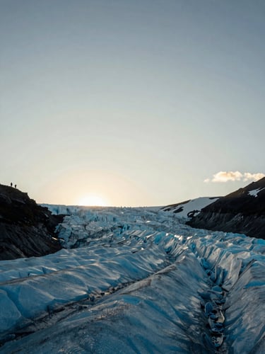 Wide panoramic shot from below looking up at a glacial valley in Patagonia at golden hour, a small silhouette of two hikers visible on a ridge in the far left third, vast sky and ice-blue light filling the frame, documentary grain, no flash