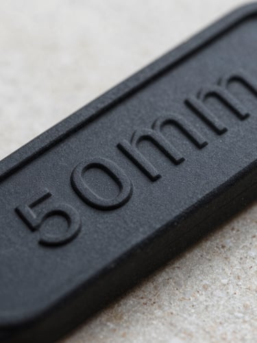 Extreme close-up macro shot of a black embossed rubber wristband on a clean neutral stone surface, sharp details of the raised lettering, soft dramatic side-lighting