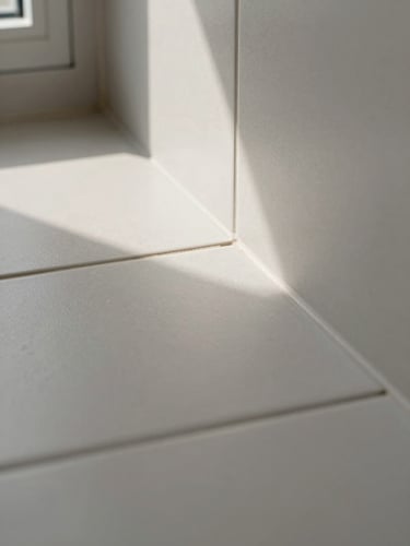 Close-up of a tile-to-floor transition in a completed bathroom — grout line sharp and uniform, tile edge flush with the threshold strip, natural window light raking across the surface to show the finish texture, no people