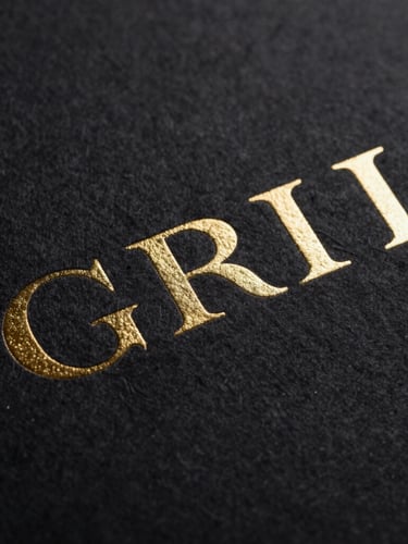 Macro photograph of embossed gold foil lettering on thick black cotton paper, sharp focus, dramatic low-key studio lighting, luxury corporate branding
