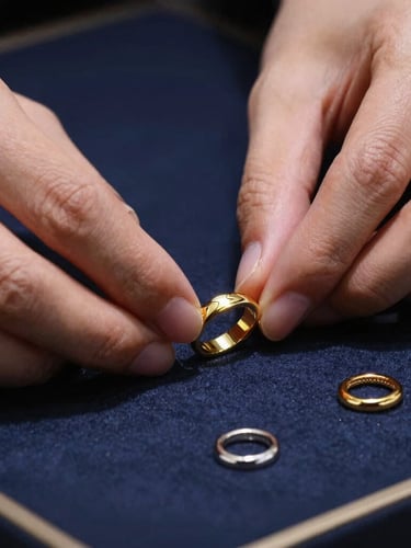 Macro shot of gold and silver jewelry reflecting dramatic studio light, professional hands carefully arranging certified pieces in a premium display case, 85mm lens
