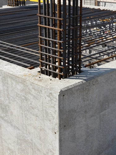 Architectural framing of a massive concrete foundation joint under high-contrast daylight, raw steel rebar visible, industrial construction photography, sharp focus, 35mm.