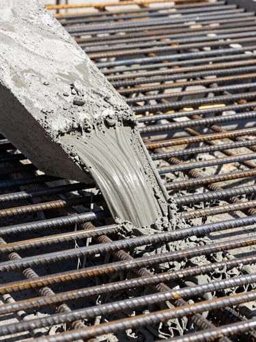 Close-up of industrial concrete pouring, wet concrete flowing over a dense grid of steel rebar, high-contrast daylight, sharp focus on structural textures