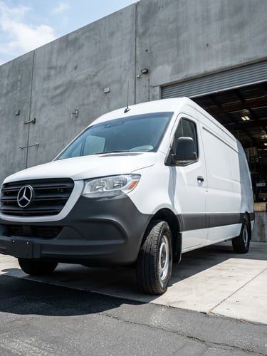 Low-angle commercial shot of a clean white cargo van parked outside a modern grey concrete warehouse bay under bright midday sun.