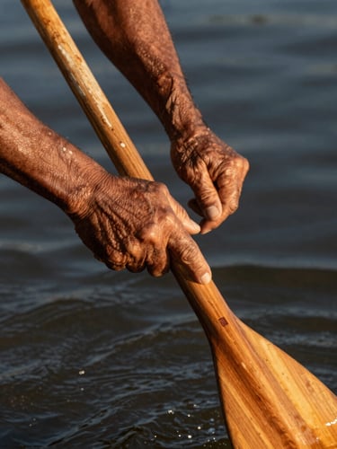 Close-up of weathered hands of a native guide holding a handmade wooden paddle over dark river water, warm afternoon sun, highly detailed texture