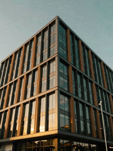 Low-angle architectural perspective of a modern eco-friendly commercial building in Lagos, warm golden-hour sunlight reflecting off structured glass and timber louvers, negative space above.
