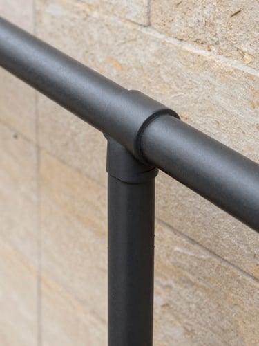 Detailed macro shot of a clean, newly installed charcoal aluminum handrail joint against warm limestone cladding, soft overcast daylight, architectural focus.