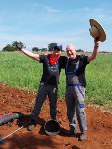Two happy male agronomists celebrating healthy soil in a sunny green field.