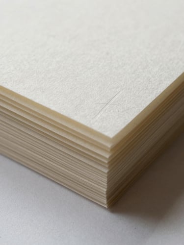 Macro shot of heavy-weight paper stocks with blind debossing, showing tactile paper fibers and crisp letterpress edges under soft northern light