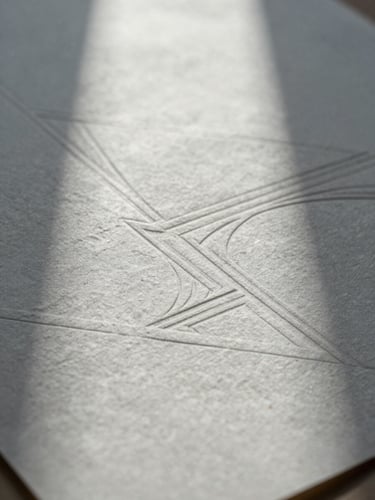 Macro shot of heavily textured handmade paper with elegant blind debossing of geometric lines, soft northern light casting cool shadows