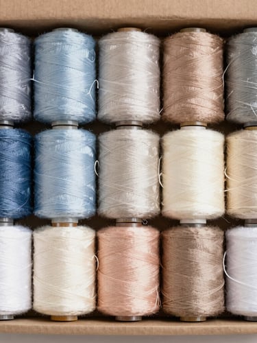 Close up of a structured cardboard box with neatly arranged spools of thread in a perfect color gradient, soft diffused light, top-down view