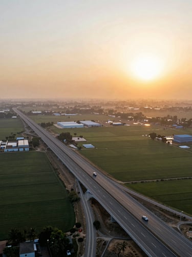 Wide panoramic aerial view of the Yamuna Expressway at sunset, showing clean multi-lane highway cutting through vast agricultural plots planned for industrial development, warm golden sunlight.