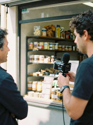 Environmental portrait of a reporter interviewing a local business owner inside a sunlit neighborhood bakery, candid moment, documentary film photography, natural ambient daylight, 35mm grain