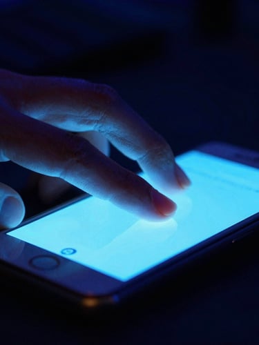 Close-up macro shot of fingers on a glowing mobile screen in a dark room, intense electric blue backlights, high-contrast tournament atmosphere, cinematic 35mm lens