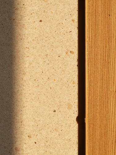 Macro texture photograph of warm, tactile travertine stone next to raw, wire-brushed oak wood. Soft golden hour light casting long, elegant shadows across the textures, medium format film style.