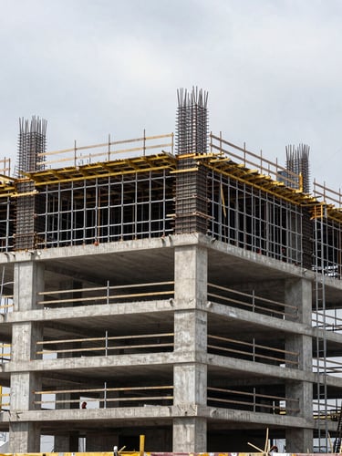 Wide site-level view of complete scaffolding and formwork installation on a reinforced concrete building under construction, overcast daylight revealing connection detail at mid-height, workers visible at scale in background, no studio lighting