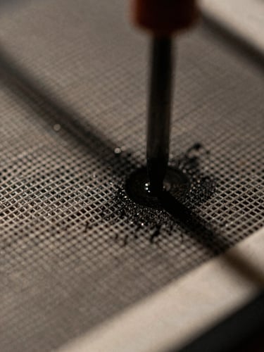 Macro close-up of ink passing through a screen mesh onto heavyweight cotton, high-contrast industrial light, gritty texture, 35mm film.