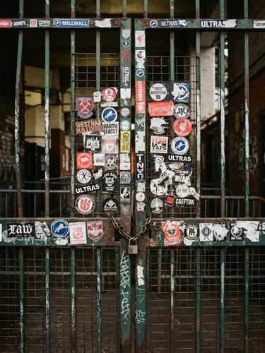 Candid 35mm film photo of an old steel stadium gate with stickers, harsh direct flash, heavy grain, overcast afternoon daylight.