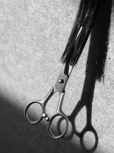 Sharp editorial black and white photography, dramatic side shadows, close-up of a precise scissor-to-hair structural cut, minimalist background