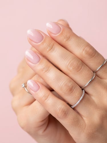 Extreme macro close-up of perfectly manicured hands with silver rings, delicate pink gel nails with subtle glitter, bright high-key studio lighting, soft powder pink background, 35mm photography