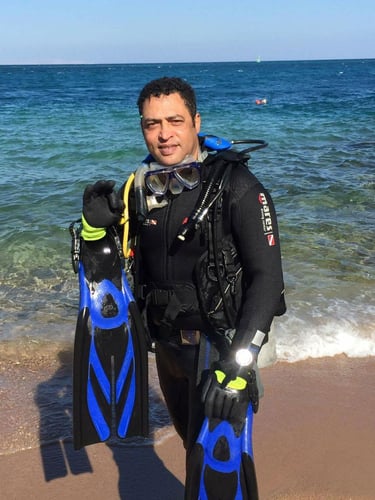 Captain Essam in a wetsuit and scuba gear standing in front of a body of
