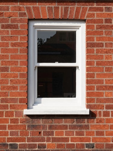 Straight-on architectural detail of a newly installed white window frame against clean red brick, sharp paint lines, bright direct daylight, highly organized composition.