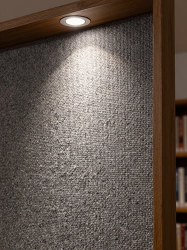 Extreme close-up of hand-woven wool panel surface in a finished library interior, warm grey twill weave structure sharp under a single hard studio strobe, architectural trim visible at the panel edge, no people, tight framing showing thread interlace