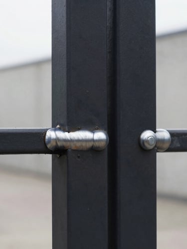 Straight frontal macro shot of a perfectly ground, seamless metal weld on a matte black steel frame, overcast soft light, architectural detail