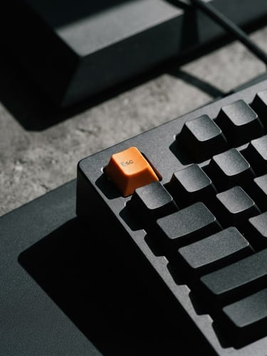 Close-up of clean mechanical keyboard setup with high-contrast studio lighting, sharp shadows, minimalist monochrome composition with a single orange keycap, 35mm photography