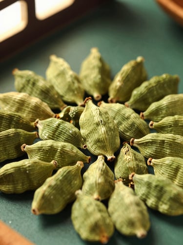 Extreme close-up of vibrant green cardamom pods and raw cinnamon bark arranged geometrically on a dark green surface, warm directional window light, shallow depth of field