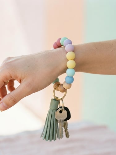 Close-up of a hand wearing a colorful silicone bead keychain wristlet, bright natural daylight, shallow depth of field, pastel background, matte texture of beads.