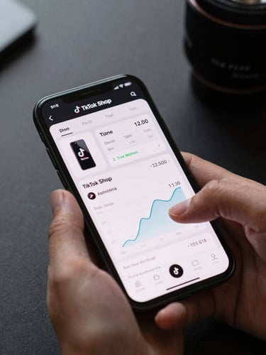 Close-up of a smartphone screen displaying a TikTok Shop product performance dashboard, real metrics and conversion rate graphs visible, hands holding the device over a clean dark desk, sharp focus on the interface data