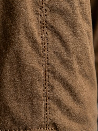 Macro close-up of a clean-finished interior seam on a heavy espresso cotton canvas jacket, showing tight, perfectly aligned parallel stitching