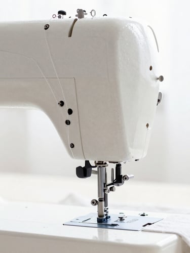 Bright high-key fashion photography, close-up of a vintage sewing machine in motion with crisp white thread, soft natural daylight, shallow depth of field