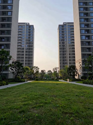 Wide environmental shot of the landscaped ground plane between four residential towers, deep green lawn and mature trees under clear morning overcast light, low horizon, no vehicles, no people, towers visible at edges framing open sky