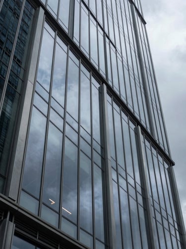 A dramatic close-up of a modern glass skyscraper facade reflecting a moody overcast sky, sharp architectural angles, cold metallic textures, vertical portrait composition.