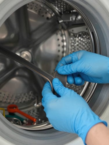 Close-up of a professional technician's hands in blue protective gloves replacing a rubber belt on a washing machine drum, bright natural light, clean tools nearby, focused editorial composition.