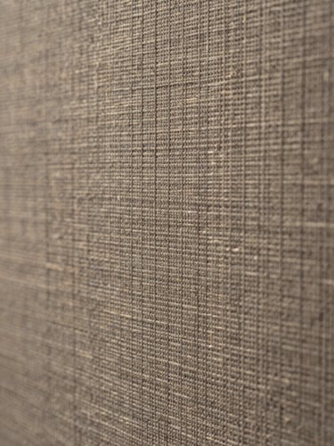 Extreme close-up of a fabric acoustic panel surface, woven textile weave texture in warm gray-tan under flat cool north-facing light, tight macro framing revealing material depth and fiber structure, no people