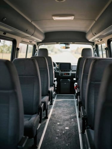 Close environmental frame, modern clean minibus interior viewed from the sliding side door, rows of dark fabric seats visible, afternoon daylight streaming through windows, no passengers, luggage area glimpsed at the rear, honest British overcast light