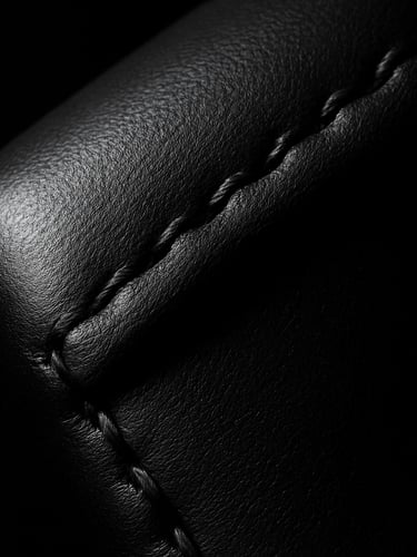 Extreme close-up shot of a pristine matte black leather edge with perfect hand-stitching, sharp directional studio light casting deep shadows, dark editorial photography style.