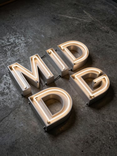 Overhead studio shot of a finished illuminated neon box sign and a set of dimensional aluminium letters arranged on a dark concrete surface, raking strobe light from the left revealing edge quality and letter depth, no people, industrial documentation style