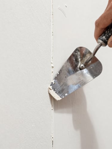 Crisp close-up of a hand using a drywall trowel to apply joint compound over a seam, bright work light, sharp focus on the smooth texture
