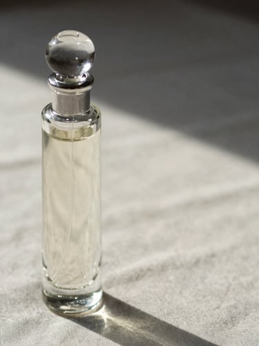 Extreme close-up of a slender glass perfume bottle resting on a pale linen surface, directional raking daylight from the left revealing the dimensional clarity of the glass stopper, generous negative space to the right, no hands, no props