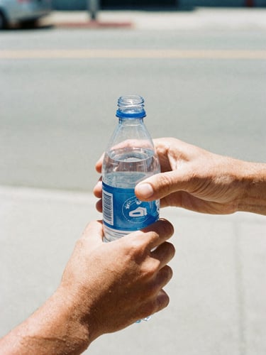 Close-up of hands handing a cold plastic bottle of water to another hand, harsh bright midday California sun, high contrast, raw documentary style, 35mm film grain