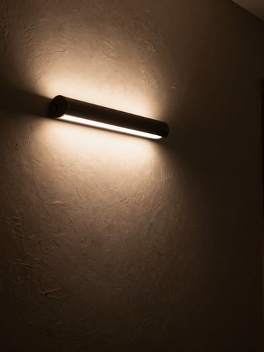 A minimalist hallway with a curved tube wall light fixture casting a warm, dramatic glow on a textured plaster wall, deep shadows, moody editorial photography.