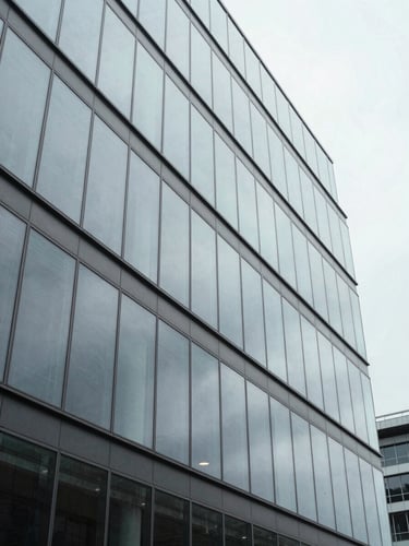Crisp wide perspective of a modern office building facade, clean glass panels reflecting a gray sky, overcast daylight, 35mm.