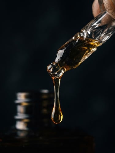Extreme macro of thick golden attar oil slowly dripping from a hand-cut crystal pipette, dramatic chiaroscuro side-lighting, deep shadows