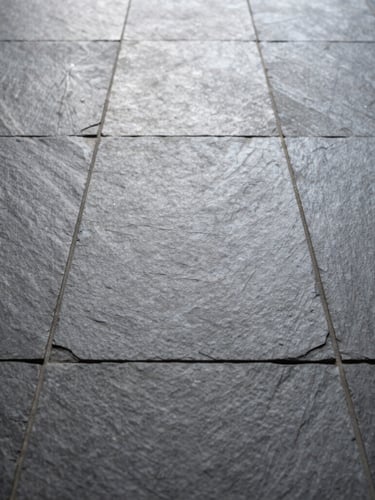 Low-angle portrait shot of pristine slate floor tiles laid in a perfect grid, natural light catching the subtle stone texture and razor-straight grout lines.